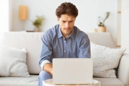 un ragazzo sta scrivendo al computer mentre è seduto sul divano