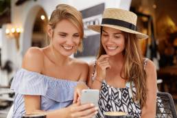 due ragazze mentre leggono le digital news del mese di agosto sul loro iPhone