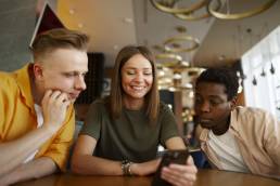 gruppo di amici seduto ad un tavolo mentre guardano contenuti sul loro iPhone