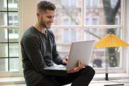 ragazzo che lavora con il suo computer seduta vicino ad una finestra