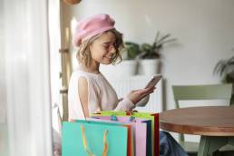 una ragazza con accanto tante buste dello shopping mentre scrivere un messaggio al cellulare