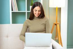 Donna con maglione verde chiaro che lavora al laptop su un divano