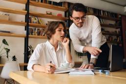 Due colleghi che discutono su un progetto, seduti in una biblioteca