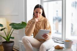 Donna seduta a casa con tablet, pensierosa durante la lettura