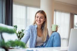 Beautiful woman freelancer noting information for planning project doing remote job via laptop computer. woman laughing while reading email on modern laptop device .