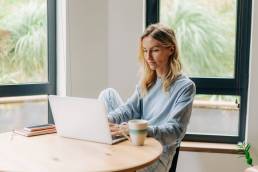 una ragazza bionda mentre seduta al tavolo lavora al computer