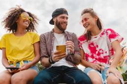 happy-young-company-smiling-friends-sitting-park-using-smartphones
