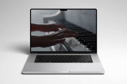Laptop su sfondo bianco che mostra un'immagine a tutto schermo di mani che suonano un pianoforte