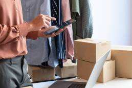 una persona mentre scrive sul suo mobile e verifica gli ordini che i suoi clienti hanno fatto online sul suo portatile