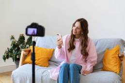 ragazza seduta sul divano mentre registra un contenuto con il suo iPhone e si riprende con una fotocamera