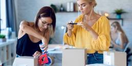 due donne imprenditrici fanno foto con lo smart-phone mentre imballano e sigillano scatole con prodotti ordinati online dai clienti la loro- tartup piccola impresa