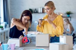 due donne imprenditrici fanno foto con lo smart-phone mentre imballano e sigillano scatole con prodotti ordinati online dai clienti la loro- tartup piccola impresa