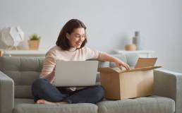 donna seduta sul divano con una portatile sulle gambe mentre apre un pacco