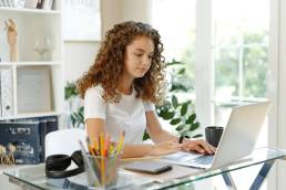 Giovane imprenditrice sorridente seduta in ufficio mentre lavora al laptop.