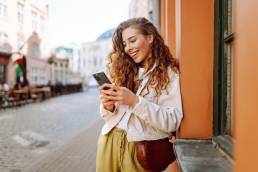 Happy woman using phone walking in city street. Lifestyle, travel, tourism, technology, blogging