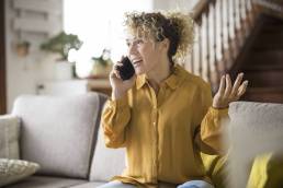 Una donna adulta felice a casa che telefona sorridendo e si gode il tempo libero seduta sul divano in uno stile di vita rilassato