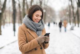 Smiling woman in winter coat using a smartphone outdoors in snow